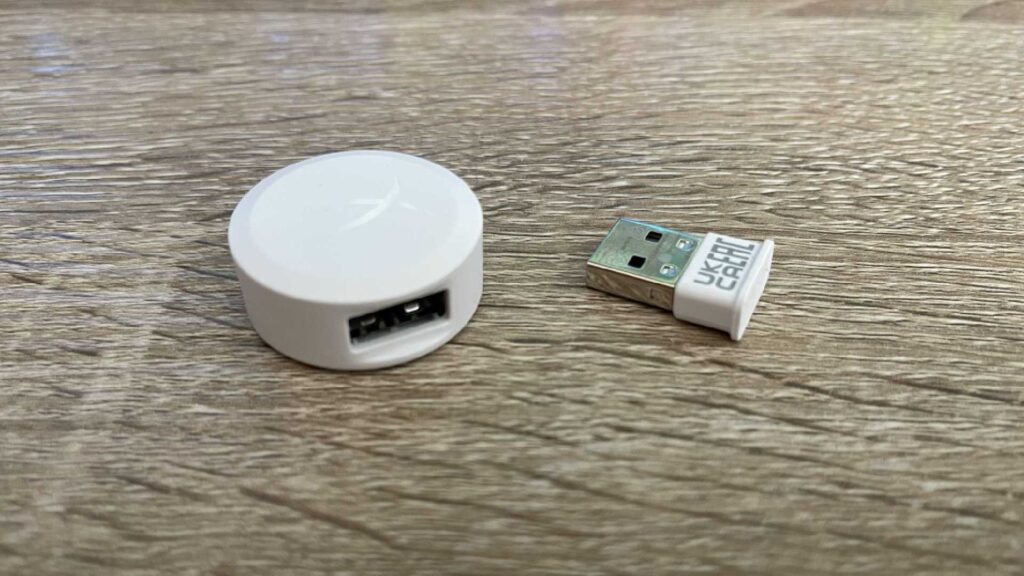 The white wireless receiver and dongle from the HyperX Pulsefire Haste 2 on an oak table.