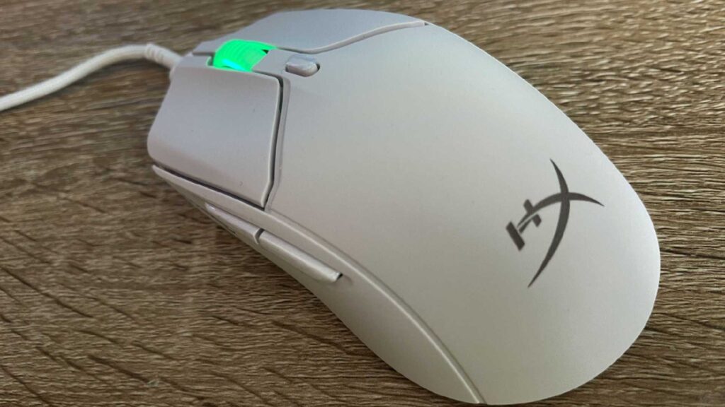 The white HyperX Pulsefire Haste 2 on an oak table. The mouse wheel is lit up in a shade of neon green.