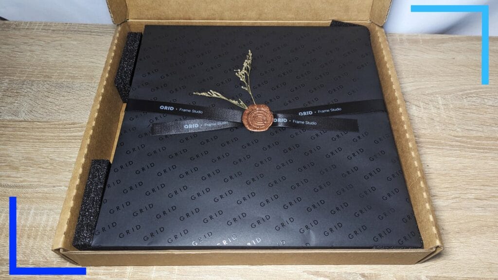 Photo of the Grid GBA wall art in a brown box with a black paper surrounding the main wall art. A brown wax seal with flowers can be seen in the center.