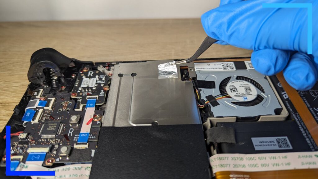 The Steam Deck silver shielding can be seen with a hand, in blue gloves, using tweezers to remove a foil sticker.