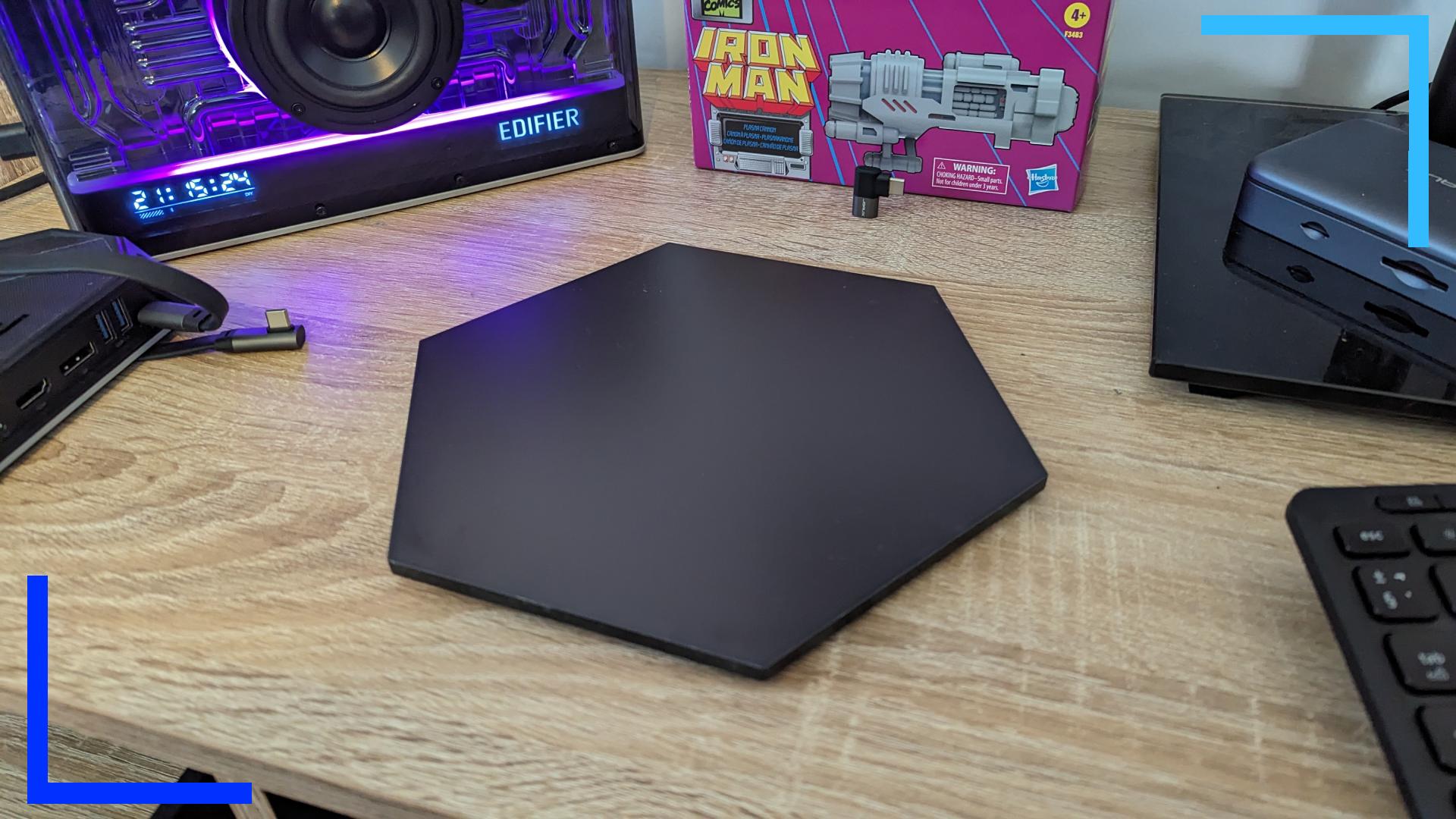 Photo of a single Nanoleaf panel on an oak desk surrounded by a set of speakers with purple lights.