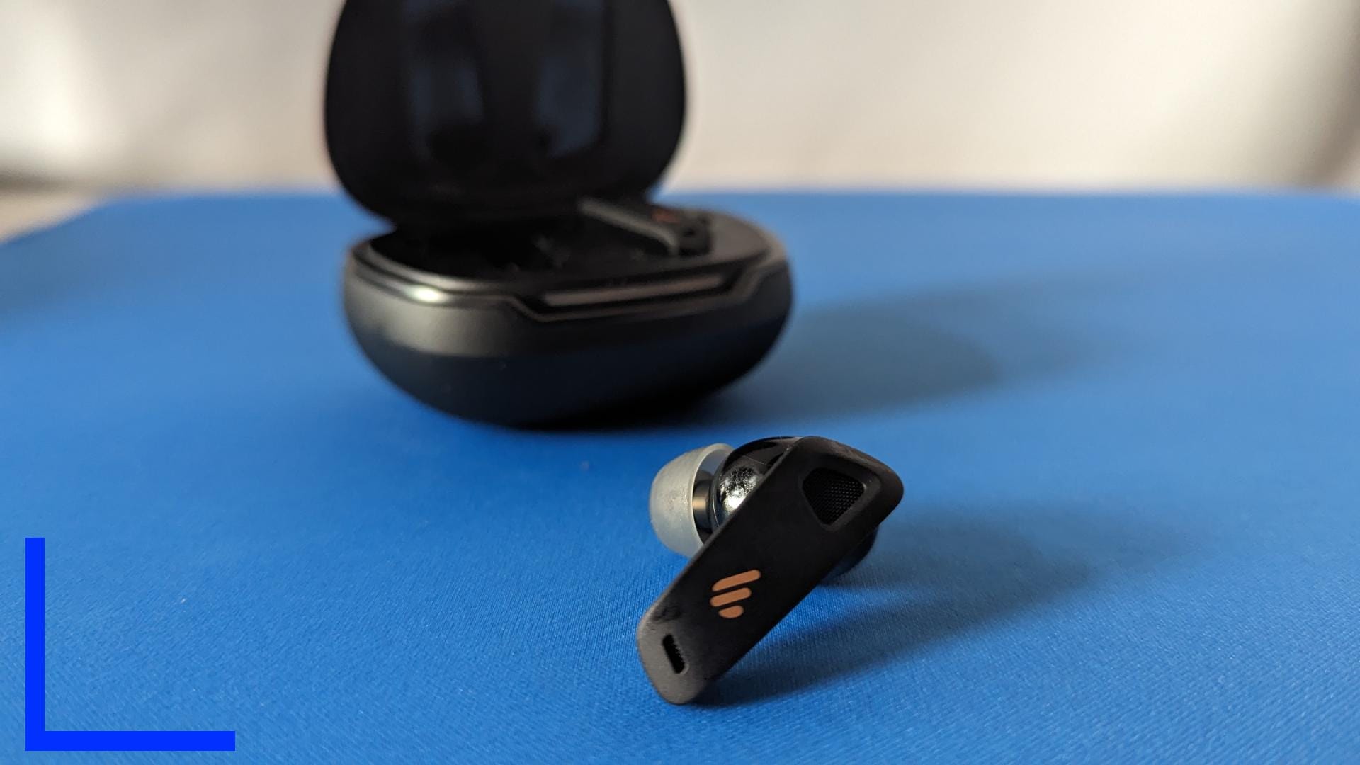 Close up photo of the left NeoBud Pro 2. In the background, the black charging case can be seen.