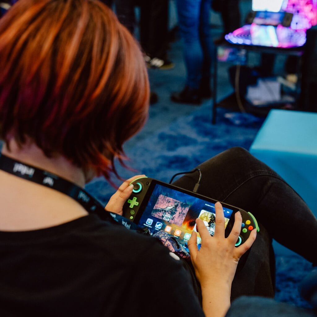 A behind shot of a red haired woman playing on the Tulpar gaming handheld.