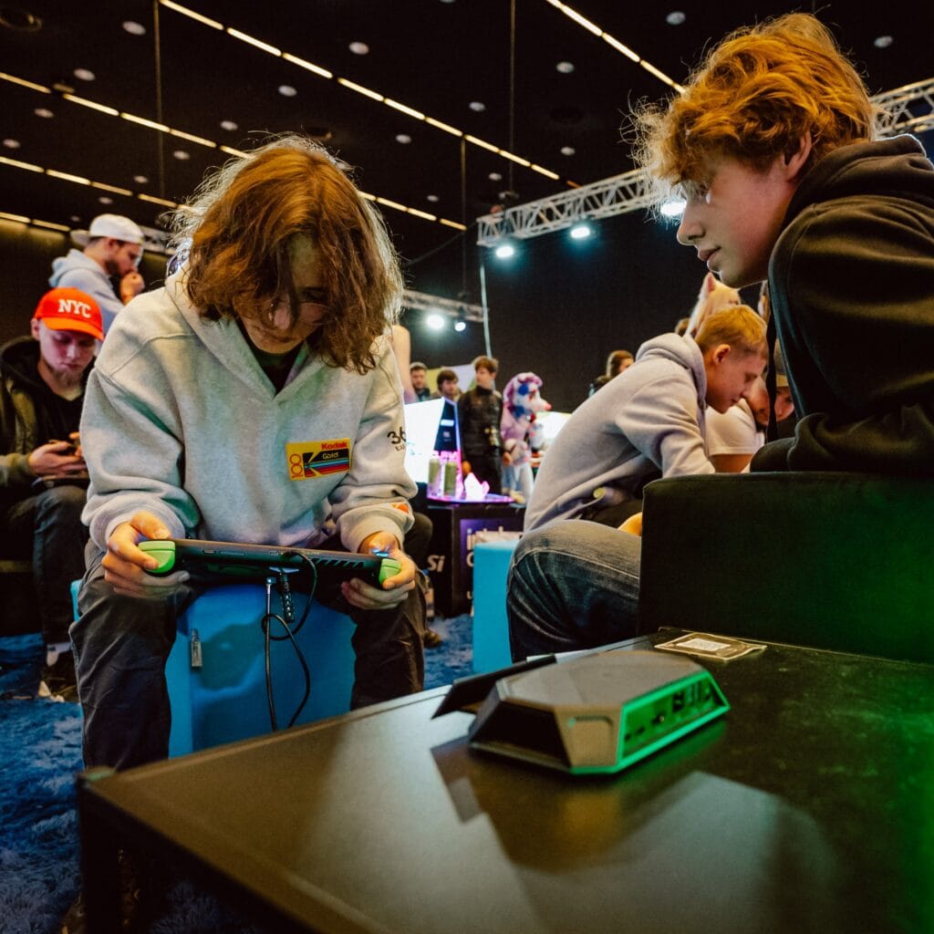 Two youngster play on the Tulpar gaming handheld. A JSAUX dock can be seen in the foreground.