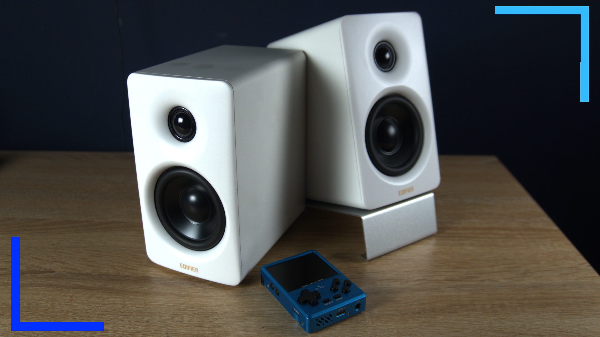 The Edifier M60 speakers in white on an okay table with a blue handheld device next to them.