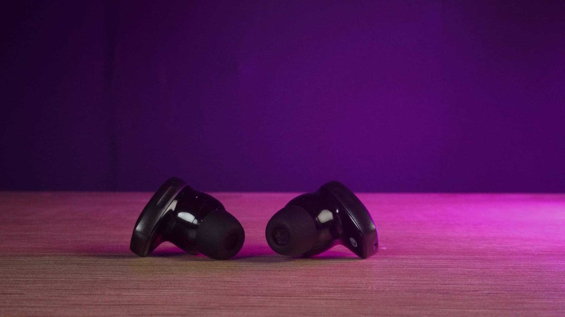 The Edifier NeoDots in black on an oak table, bathed in a pink light.